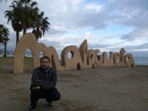 Nico, el autor del artículo, agachado frente a las letras que forman la palabra MALAGUETA, en la playa de Málaga